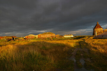 Golden rural landscape on Solovetsky Island with wooden houses, fields and dramatic storm clouds at sunset.