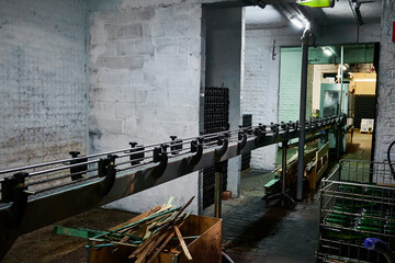 Industrial bottling line. The photo shows the conveyor system used for filling and transporting beer bottles in a traditional brewery setting with exposed brick walls and soft lighting.