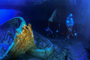 Scuba divers explore the deep wreck of the Salem Express, illuminated by blue ambient light and surrounded by corroded metal structures on the seafloor.