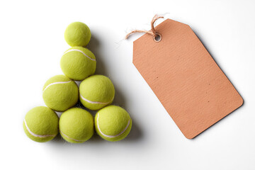 Seven bright tennis balls arranged in a triangular stack beside a blank cardboard tag on a clean white background.