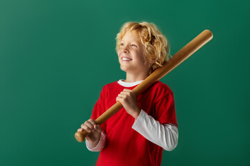 Cheerful boy in red clothes poses with a baseball bat against a green backdrop