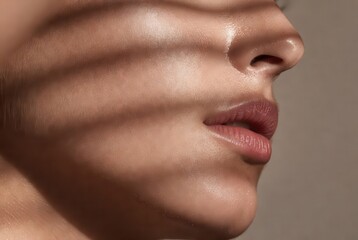 Side view close-up of a person's face with dramatic linear shadows and a healthy glow