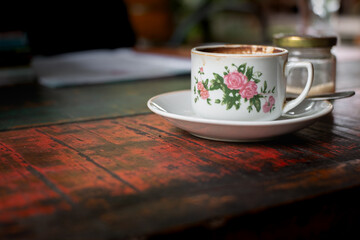 Perfect cup of black coffee served with a spoon and bottle of sugar on a simple white plate at red wooden table in a cafeteria.