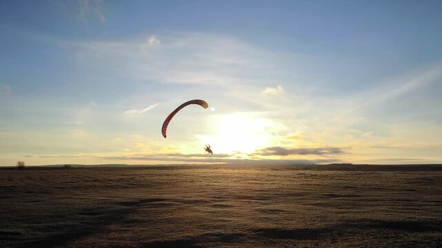 A pilot on a motorized paraglider flies over a deserted field against a background of soft dawn and clouds. The concept of freedom, travel and extreme sports.
