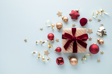 Golden gift or present box with velvet red ribbon with festive decoration on light blue background...