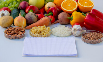 Blank notepad for writing a diet plan against a background of fruits, vegetables, and grains