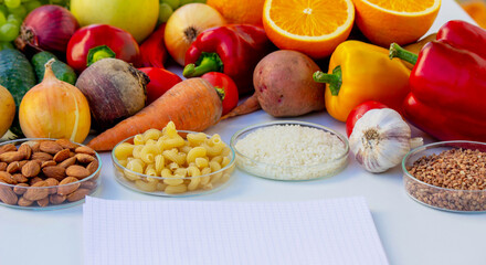 Blank notepad for writing a diet plan against a background of fruits, vegetables, and grains