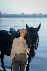 Obraz premium An adult woman holding a black horse and standing near the river