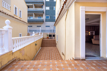 Obraz premium Sunny Mediterranean patio with tiled flooring, white balustrade, and stairs to residential entrance