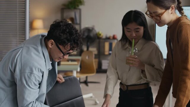 Tilt down shot of three young Asian coworkers standing by desk while analyzing business charts in modern office space