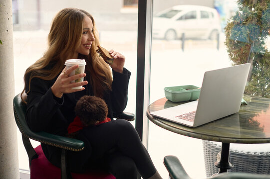 Woman Eating Sandwich and Drinking Coffee While Working in Café