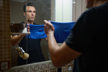 Man Grooms in Bathroom Mirror Holding Blue Towel While Working From Home as Entrepreneur and Father