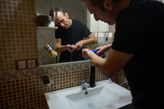 Man In Black T-Shirt Brushing Teeth At Bathroom Mirror While Working From Home