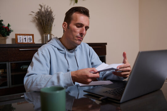 Focused Home Office Worker Reviews Papers While Working Remotely On Laptop - Powered by Adobe