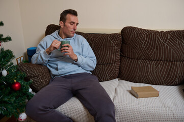 Fototapeta premium Relaxed Father Working From Home On Couch With Coffee Near Christmas Tree