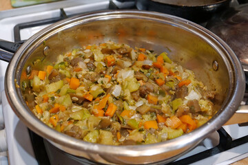 Vegetable stew is cooked on gas stove. Ragout is cooked in metal pan