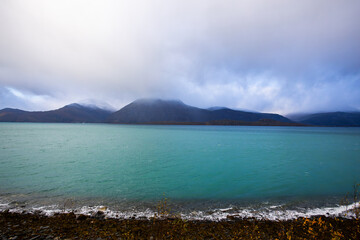 Autumn landscape of the Lyngen Alps in Northern Norway with snowy peaks, dramatic clouds, and a tranquil fjord.