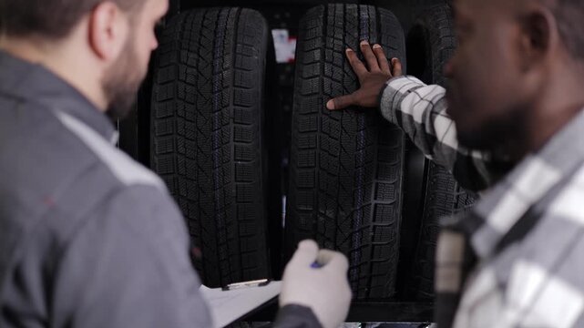 African young adult male choosing tires with salesperson in store.