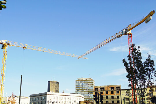 Two tower cranes operating at a construction site against the backdrop of a cityscape that combines historical and modern architecture. Illustrates urban renewal and metropolitan expansion.
