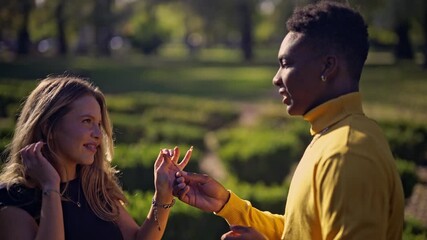 A happy diverse couple enjoys a sweet and romantic moment in a sunny green park, sharing a playful interaction with a sprig before embracing warmly. - Powered by Adobe