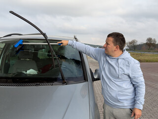Man cleaning car windshield with a brush in a parking lot.