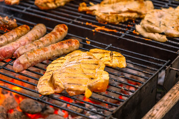 Close-Up of Chicken Steaks and Sausages Grilling on a Hot Barbecue Rack Over Red Hot Coals and Flames.