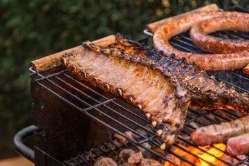 Appetizing Marinated Pork Ribs and Sausages Grilling on a Barbecue Rack over Glowing Coals and Flames