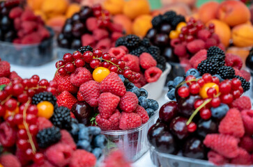 Prague, czech republic, august 9, 2023. Assortment of fresh organic berries including raspberries, blueberries, red currants, strawberries, and cherries in plastic containers at a market