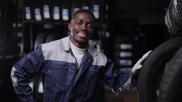 Portrait happy African male mechanic smile and giving thumbs up in garage workshop or tyre store, dark background.