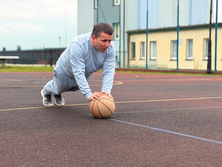 A man in athletic clothing performing a push-up on a basketball court using a basketball