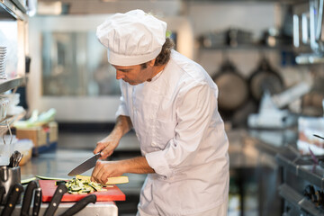 Adult male chef in uniform chops ingredients for dish in restaurant kitchen