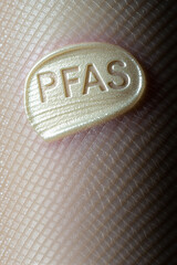 A macro photograph captures a glossy, pale yellow patch labeled "PFAS" resting on a finely textured, skin-like surface with a grid pattern.