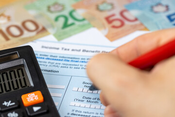 Income tax and benefits in Canada. Financial business concept. Hand-filling a paper tax return, Canadian dollars, calculator. Tax calculations