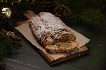 Slices of German Christmas stollen cake on a wooden cutting board on rustic background with lights and decorations. Traditional handmade Christmas dessert. Fruit bread with nuts, raisins and marzipan.