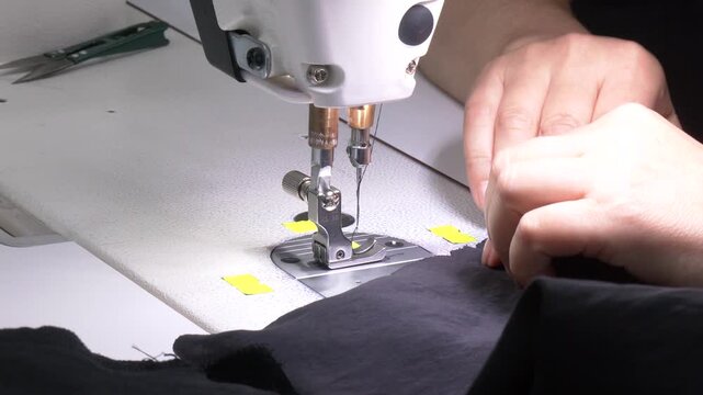 Fingers hand of seamstress with needle presser foot and thread of industrial sewing machine to sew seam of black cloth close-up. Hands of young girl on sewing machine
