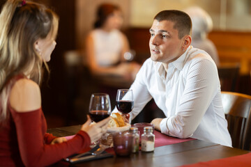 Happy young couple enjoying relaxed dinner together in cozy restaurant while talking and sharing wine