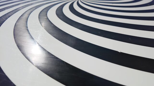 A high‑gloss paneled surface featuring a hypnotic Op Art spiral made of alternating black and white curved bands.