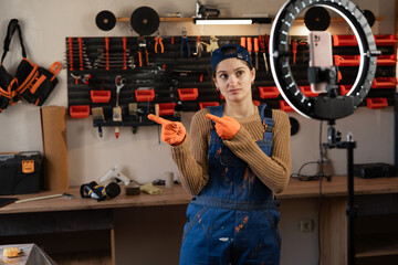 Repairman or Handyman blogger streaming in workshop with assortment tools use smartphone, point index fingers aside indicate area copy space. Blogging, industry and technology