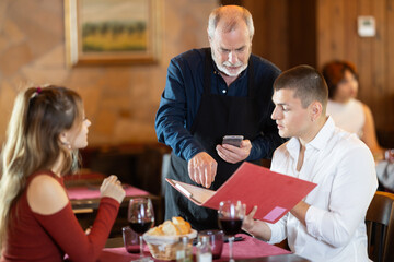 Attentive senior waiter taking order from young couple during relaxed dinner in comfortable restaurant setting