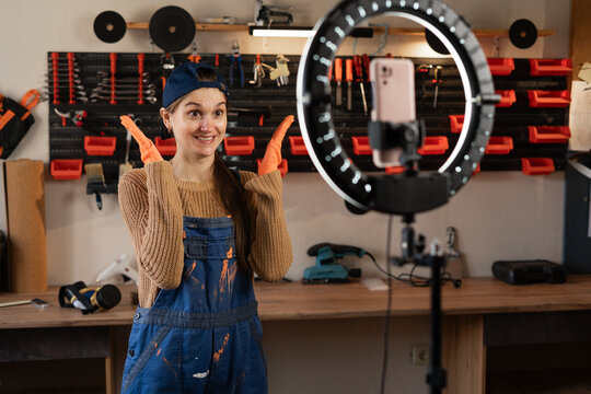 Joyful Repairman or Handyman blogger streaming in workshop with assortment tools use smartphone holding raised arms has amazed facial expression. Blogging, industry and technology