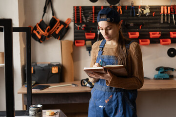 Job occupation concept. young female worker in uniform holding notepad in her carpentry workshop.