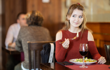 Young woman having dinner, drinking wine and eating salad in restaurant