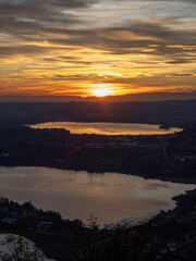 A breathtaking aerial view of the sunset over the two Brianza lakes (Annone and Pusiano) in Lombardy, Italy, with mountains silhouetted on the horizon. 