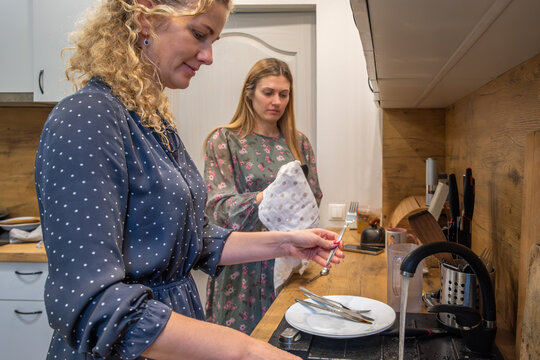 Two women preparing a meal in a modern kitchen, one arranging utensils while the other holds a towel, showcasing a collaborative cooking experience with healthy food preparation
