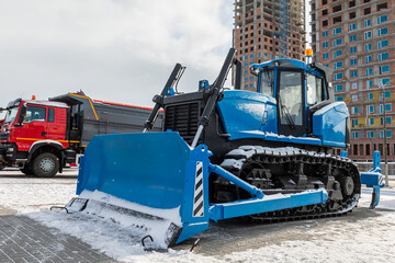 A blue bulldozer and a dump truck at a construction site in winter