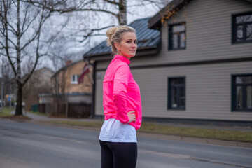 Woman with curly hair wearing a bright pink jacket stands confidently outdoors, showcasing a...