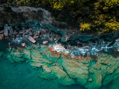 Drone view of rocky coastline with turquoise water and forest edge. Bright and cinematic tropical seascap