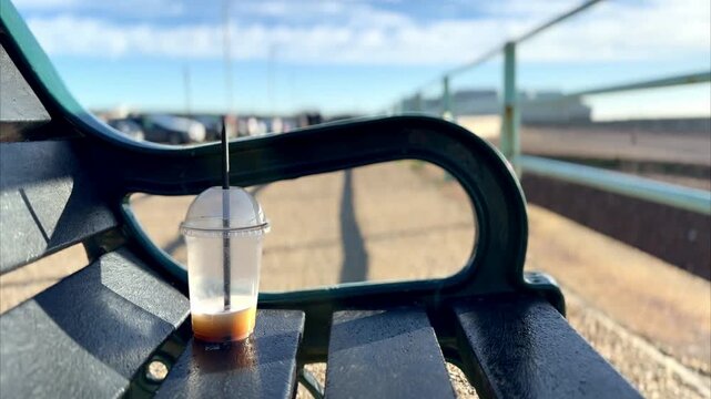 view of half drunk iced coffee drink in plastic cup litter left on public bench