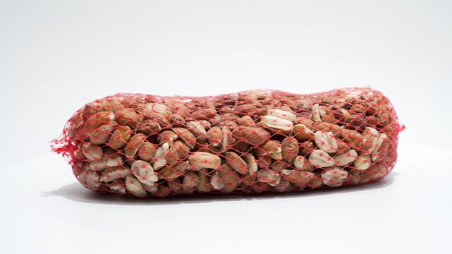 Mesh bag of mixed nuts bird food rotates on a white background. Close-up highlights peanut pieces and kernels inside the net.