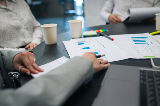Businesspeople analyzing printed charts and bar graphs during meeting, close-up view of hands and documents